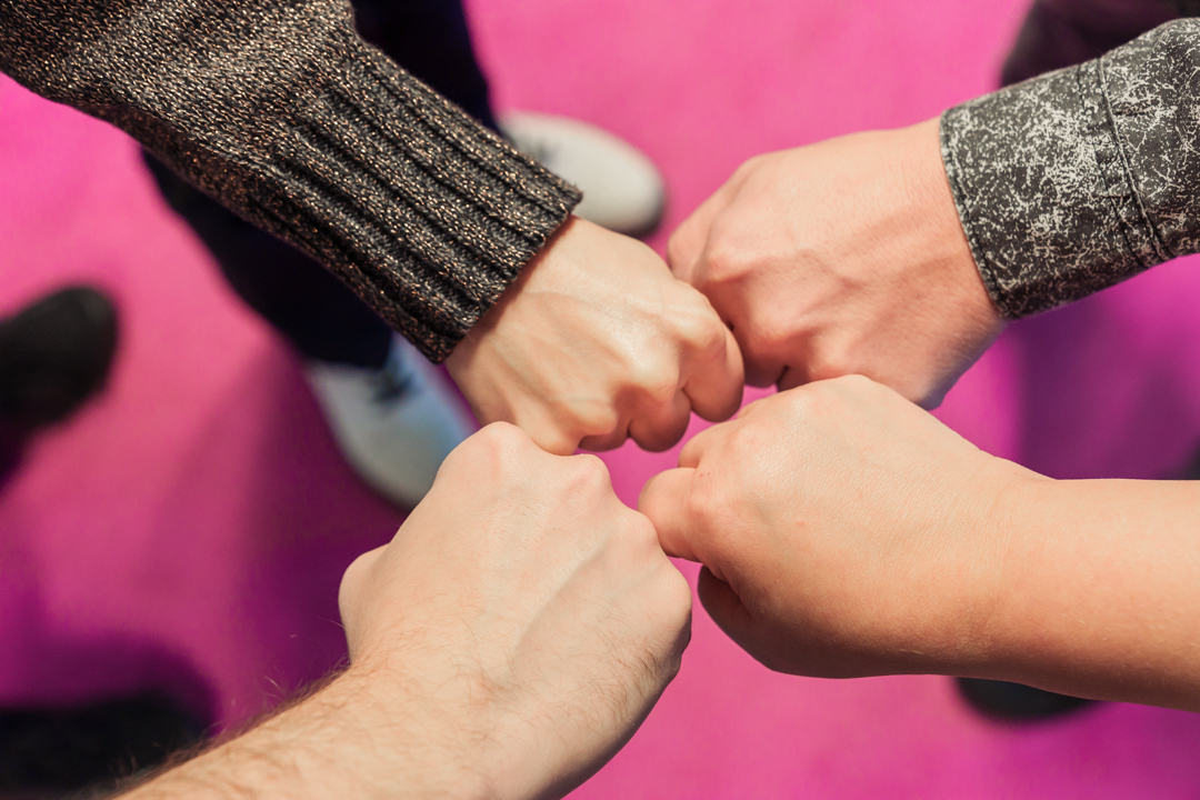 Kuvituskuva: neljä kättä nyrkissä vastakkain ystävyyden merkiksi