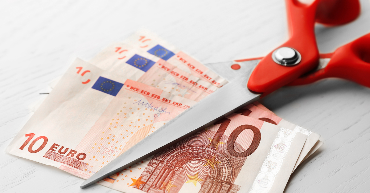 Punaiset sakset leikkaamassa 10 euron seteleitä.