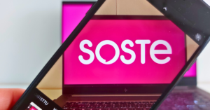 Kannettavalla tietokoneella näkyvä SOSTEn logo puhelimen ruudun kautta kuvattuna.