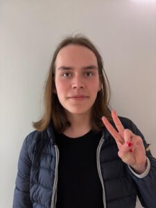 Verso Vuorenmaa katsoo rennoissa vaatteissa kameraan ja näyttää sormilla rauhanmerkkiä